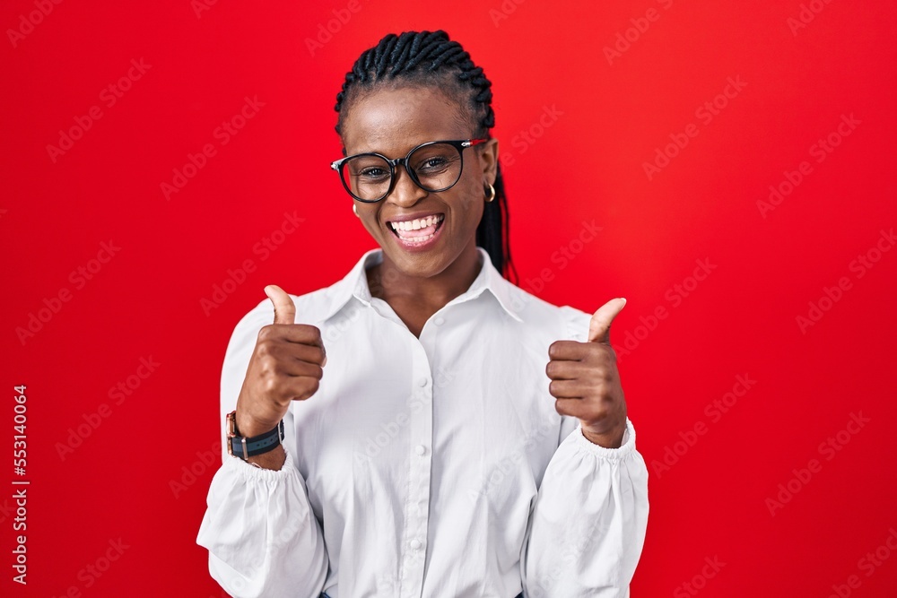 African woman with braids standing over red background success sign doing positive gesture with hand, thumbs up smiling and happy. cheerful expression and winner gesture. African woman with braids standing over red background success sign doing positive gesture with hand, thumbs up smiling and happy. cheerful expression and winner gesture.