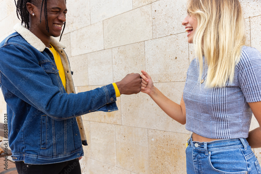 Friends giving fist bump together standing in front of wall Friends giving fist bump together standing in front of wall