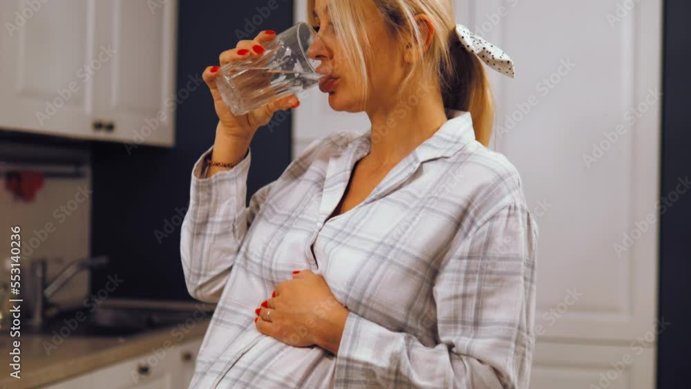 Happy peaceful attractive young pregnant woman drinking glass of fresh