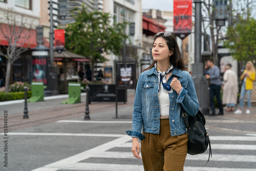 Fototapeta premium Asian Korean girl carrying a bag and wearing sunglasses on her head crossing the road in leisurely afternoon. real life concept