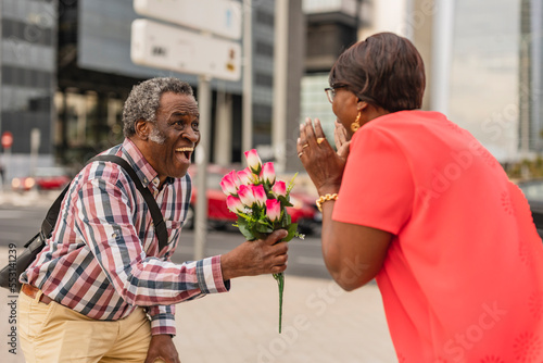 Senior man surprising woman with bunch of flowers