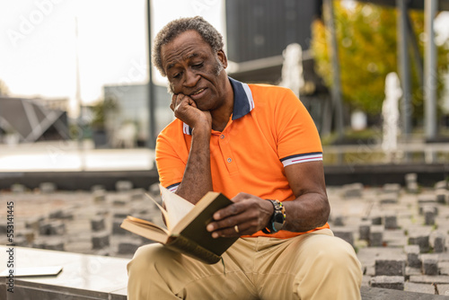 Senior man with hand on chin reading book photo