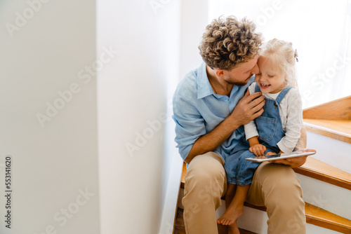 Young father and his daughter using tablet computer on stairs at home