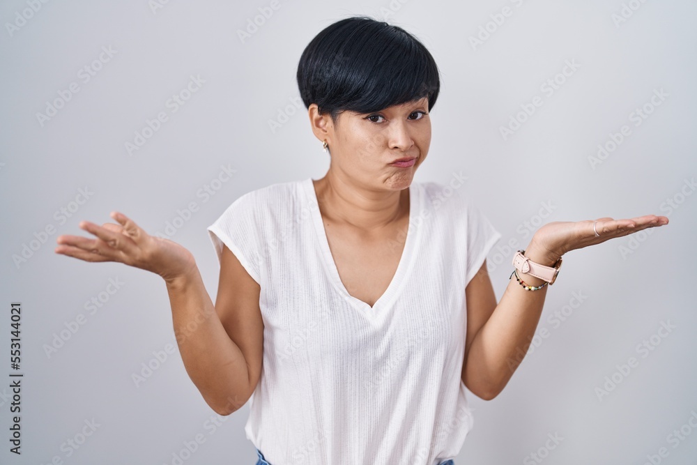 Young asian woman with short hair standing over isolated background clueless and confused expression with arms and hands raised. doubt concept. Young asian woman with short hair standing over isolated background clueless and confused expression with arms and hands raised. doubt concept.