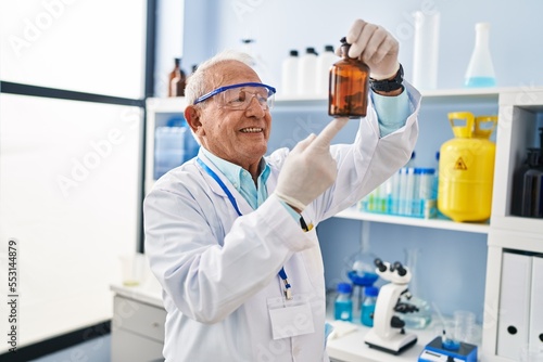 Senior man wearing scientist uniform holding bottle at laboratory