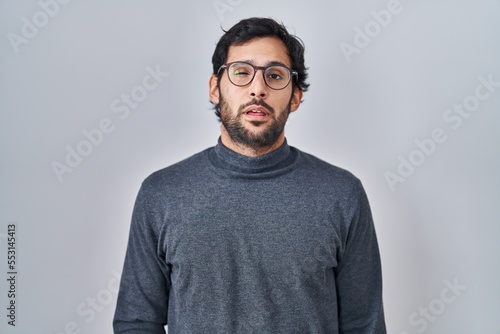 Handsome latin man standing over isolated background looking sleepy and tired, exhausted for fatigue and hangover, lazy eyes in the morning.