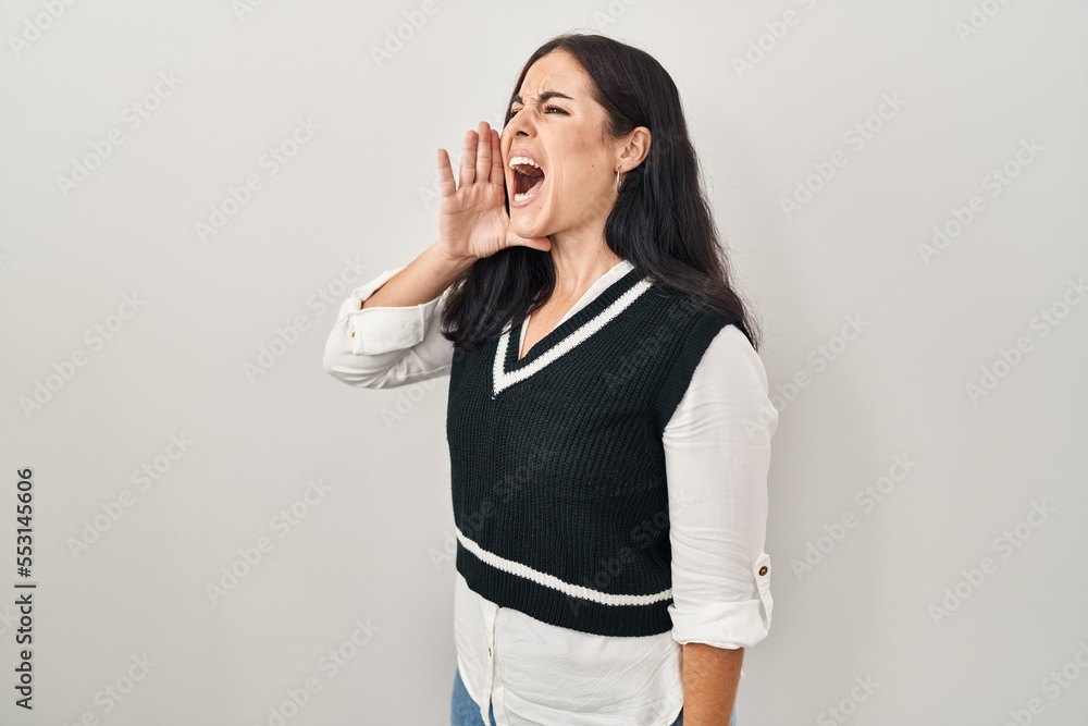 Young hispanic woman standing over isolated background shouting and screaming loud to side with hand on mouth. communication concept. Young hispanic woman standing over isolated background shouting and screaming loud to side with hand on mouth. communication concept.