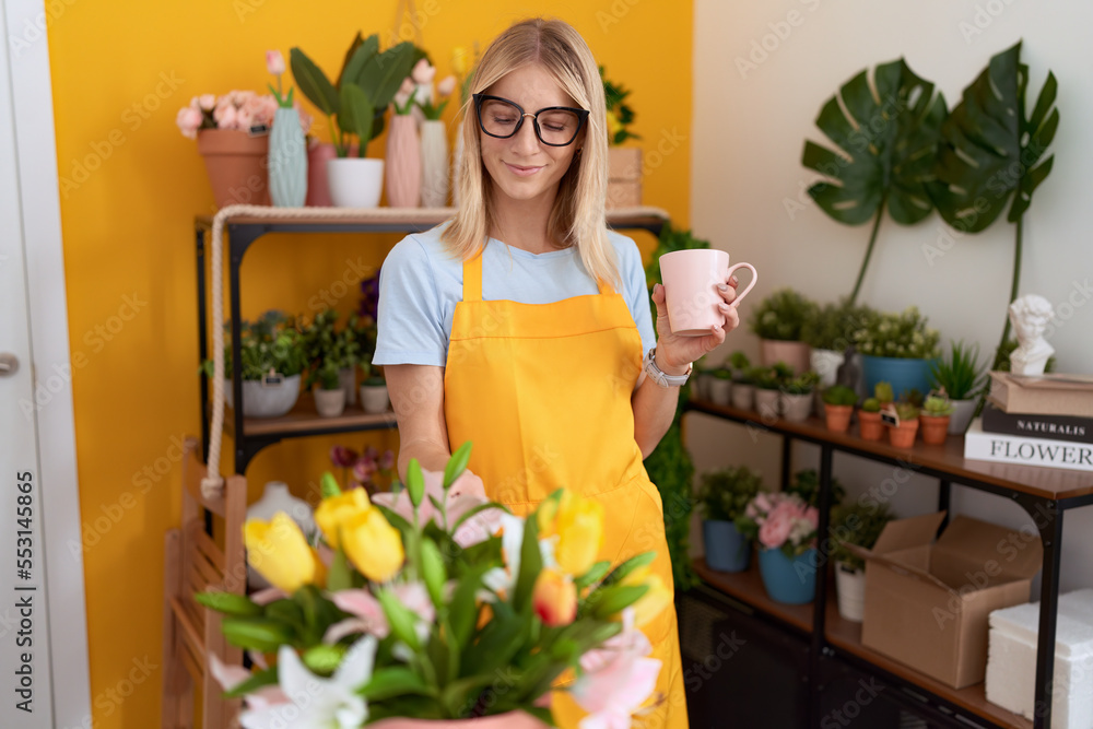 Young blonde woman florist smiling confident drinking cup of coffee at flower shop