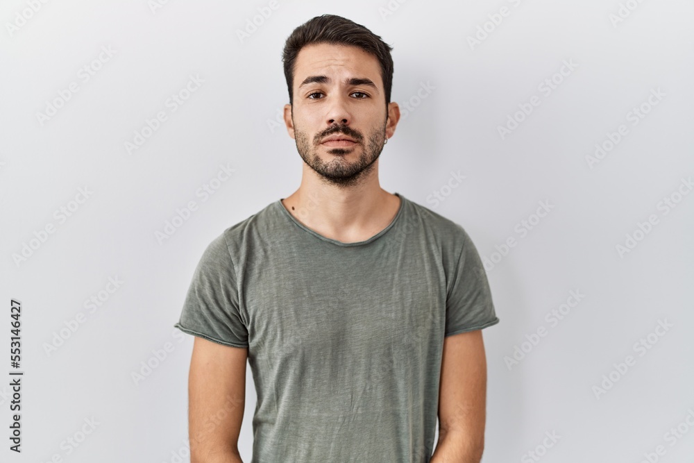Young hispanic man with beard wearing casual t shirt over white background relaxed with serious expression on face. simple and natural looking at the camera. Young hispanic man with beard wearing casual t shirt over white background relaxed with serious expression on face. simple and natural looking at the camera.