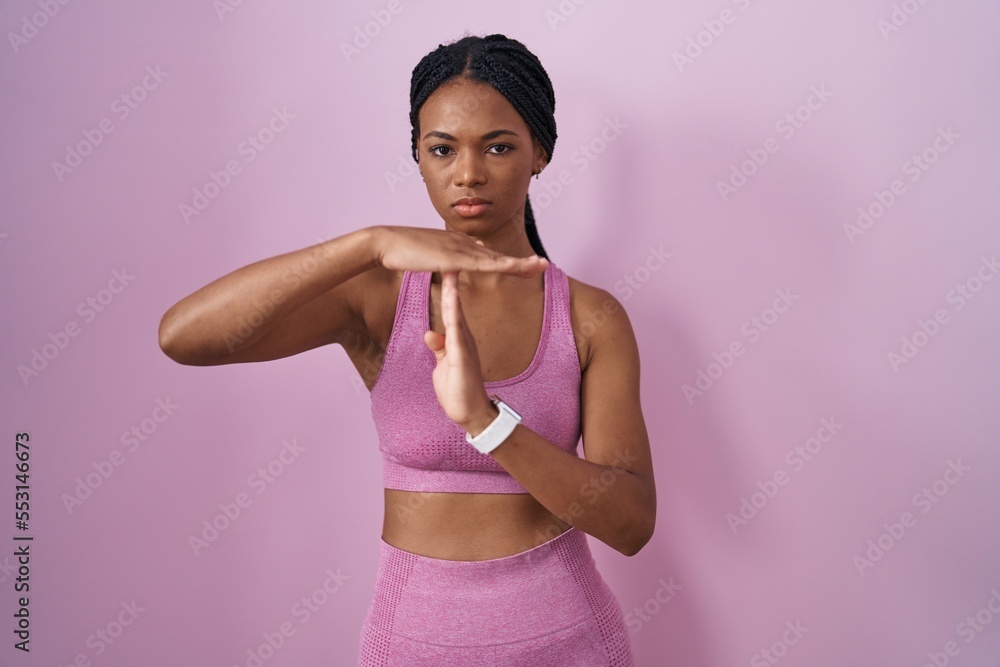 African american woman with braids wearing sportswear over pink background doing time out gesture with hands, frustrated and serious face