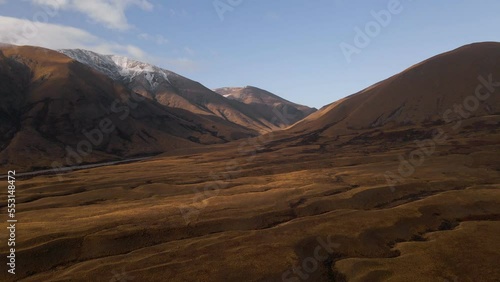 Aerial - golden, wavy plains in front of snow capped hills in Mackenzie, New Zealand photo