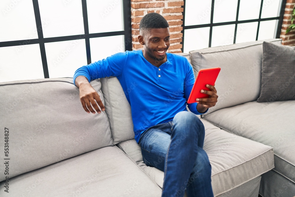 Young african american man using touchpad sitting on sofa at home