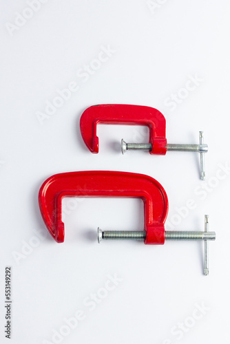 Two red metal clamps of different sizes on a white background. Tools for repair work and DIY projects. Construction, craft, work with wood products.