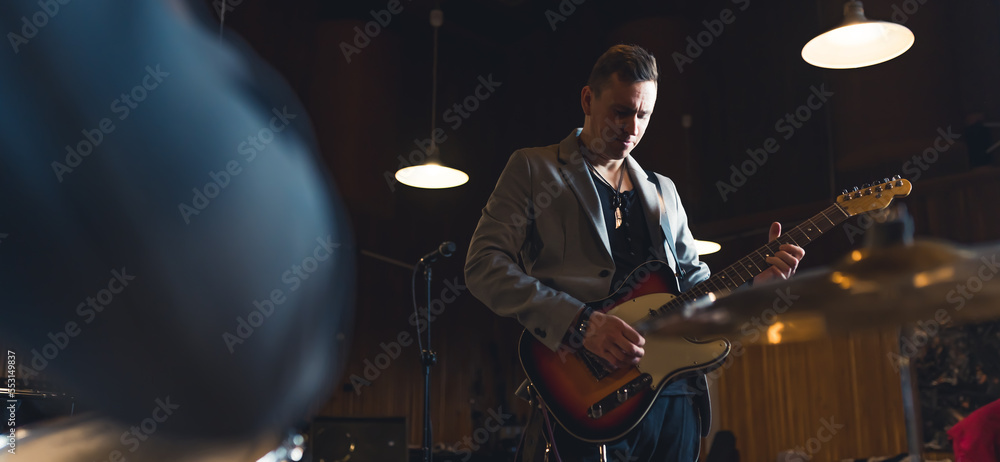 Obraz premium Bassist with his guitar. Wide indoor shot of caucasian mid adult male musician in grey blazer playing on his guitar. High quality photo