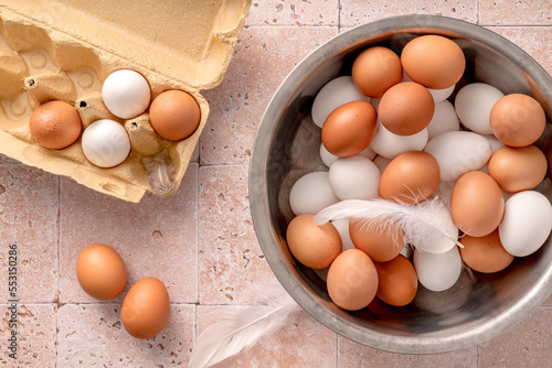 Eggs in metallic bowl on beige background. Top view of raw brown eggs and white eggs in open egg box.