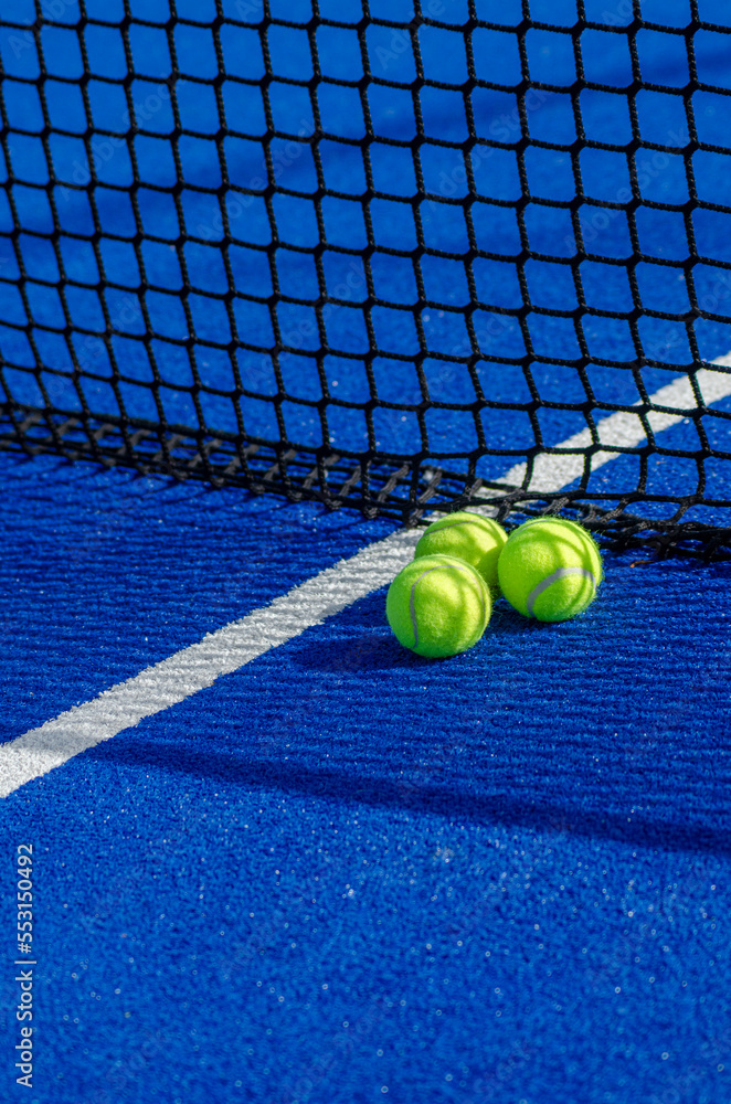 three balls close to the net of a blue paddle tennis court