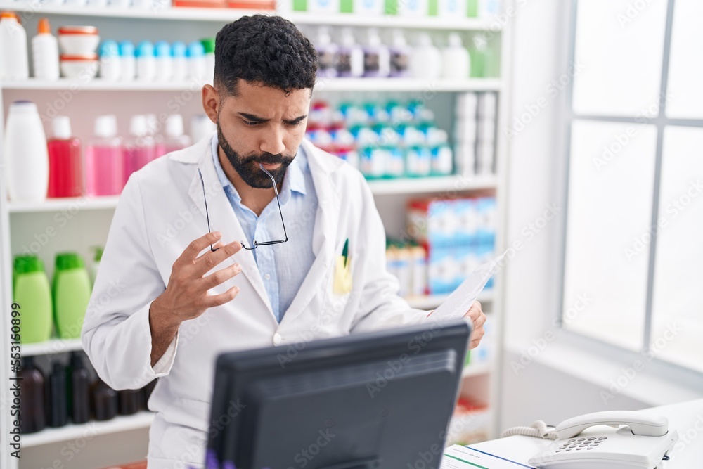 Young arab man pharmacist reading document with doubt expression at pharmacy