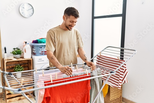 Young hispanic man smilig confident hanging clothes at laundry room photo