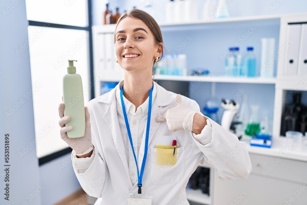 Young caucasian woman working at scientist laboratory holding body lotion pointing finger to one self smiling happy and proud Young caucasian woman working at scientist laboratory holding body lotion pointing finger to one self smiling happy and proud