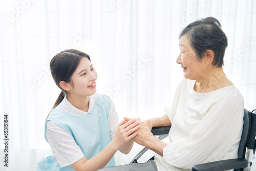 車椅子に乗る高齢者女性と会話する介護士