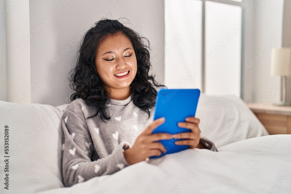 Young chinese woman using touchpad sitting on bed at bedroom Young chinese woman using touchpad sitting on bed at bedroom