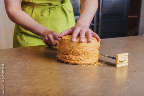 Female baker slicing traditional sponge cake into layers using special cake knife. DIY, sequence, step by step.