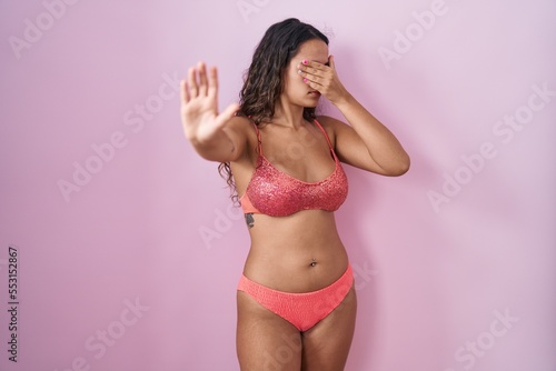 Young hispanic woman wearing lingerie over pink background covering eyes with hands and doing stop gesture with sad and fear expression. embarrassed and negative concept.