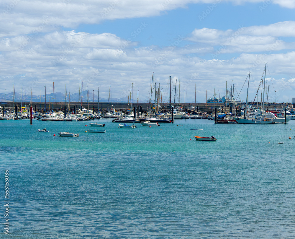 Obraz premium The bay and part of the port of Corralejo with boats, surf school, houses and mountains in the background, Spain