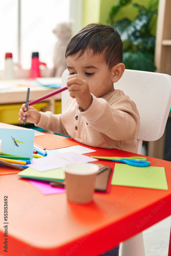 Adorable hispanic toddler student drawing on notebook at kindergarten Adorable hispanic toddler student drawing on notebook at kindergarten