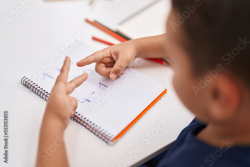 Adorable hispanic toddler doing mathematics exercise counting with fingers at classroom