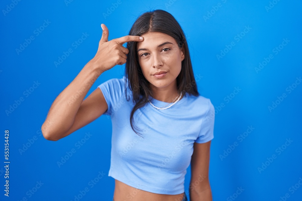 Brunette young woman standing over blue background pointing unhappy to pimple on forehead, ugly infection of blackhead. acne and skin problem Brunette young woman standing over blue background pointing unhappy to pimple on forehead, ugly infection of blackhead. acne and skin problem