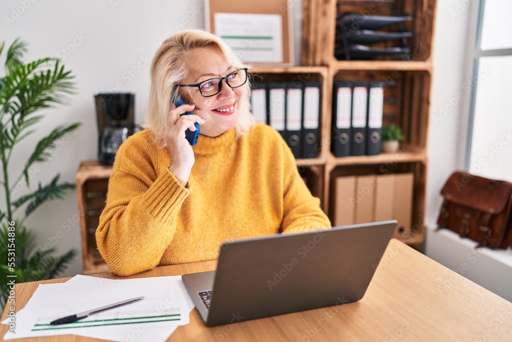 Φωτογραφία Middle age blonde woman businesswoman talking on the smartphone working at offic