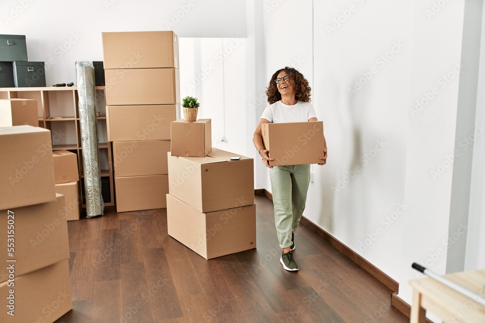 Middle age hispanic woman smiling confident holding cardboard box at new home Middle age hispanic woman smiling confident holding cardboard box at new home