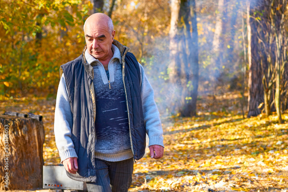 Cheerful elderly man pensioner makes a fire for grilling at a picnic in autumn Cheerful elderly man pensioner makes a fire for grilling at a picnic in autumn