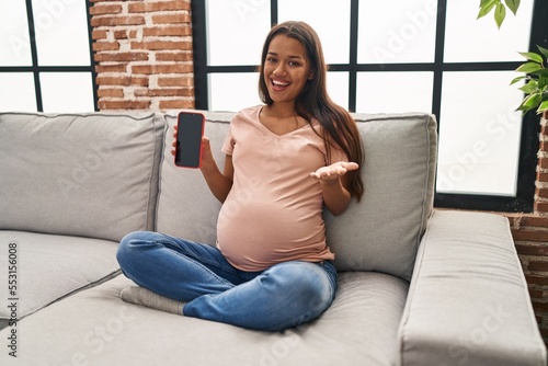 Young pregnant woman holding smartphone showing screen celebrating achievement with happy smile and winner expression with raised hand