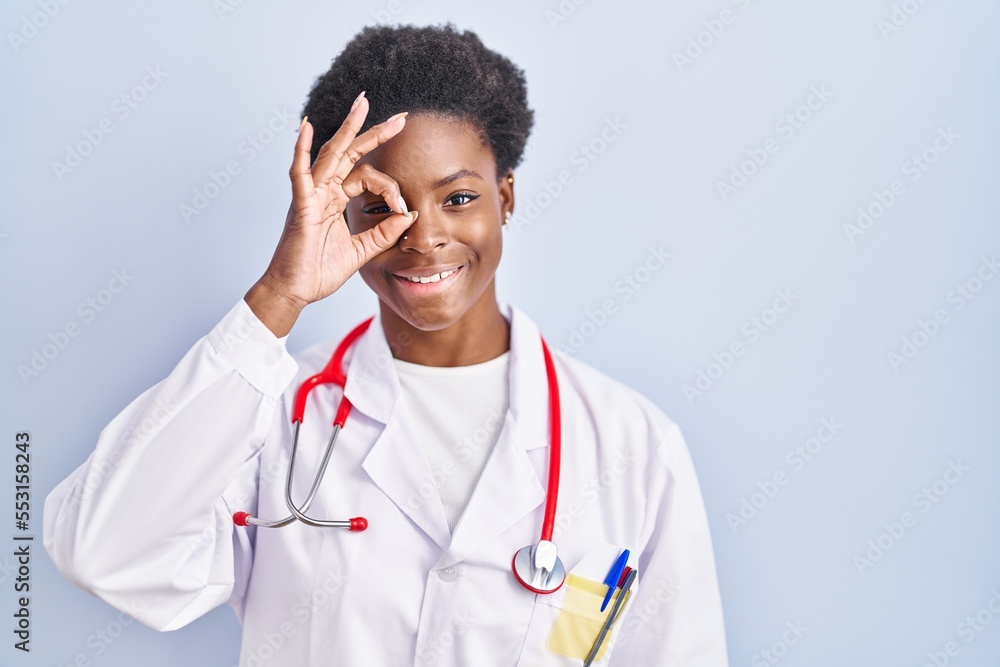 African american woman wearing doctor uniform and stethoscope smiling happy doing ok sign with hand on eye looking through fingers African american woman wearing doctor uniform and stethoscope smiling happy doing ok sign with hand on eye looking through fingers