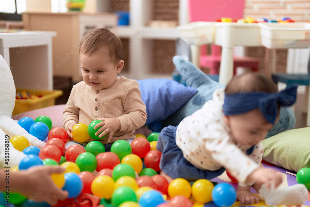 Two toddlers playing with balls sitting on floor at kindergarten Two toddlers playing with balls sitting on floor at kindergarten