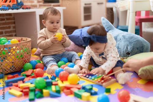 Two toddlers playing with balls and xylophone sitting on floor at kindergarten