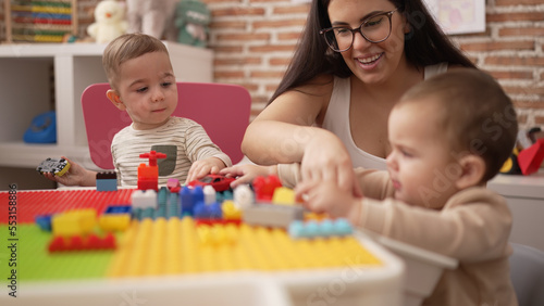 Teacher and preschool students playing with construction blocks sitting on table at kindergarten