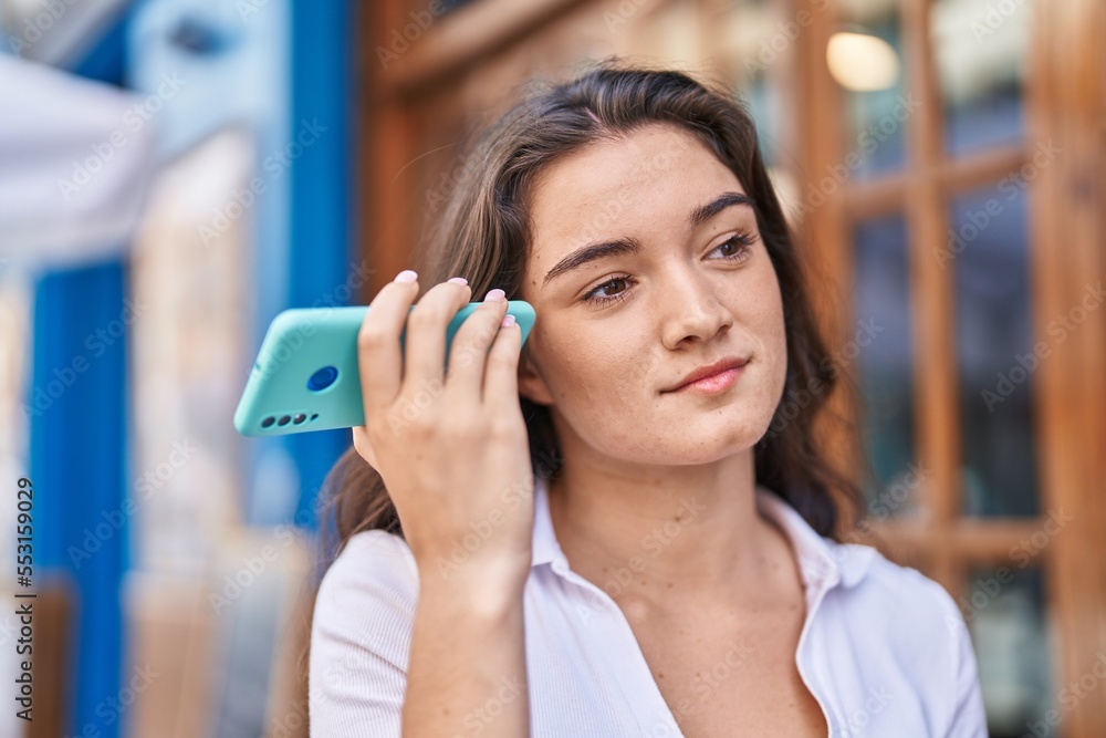 Young hispanic woman listening audio message by the smartphone at street