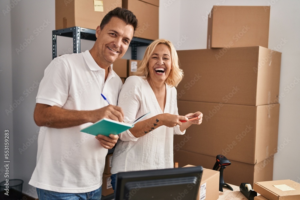 Middle age man and woman business partners scanning label using smartphone working at storehouse Middle age man and woman business partners scanning label using smartphone working at storehouse