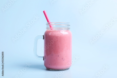 Mason jar with delicious berry smoothie on light blue background