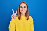 Young woman standing over blue background showing and pointing up with fingers number two while smiling confident and happy.