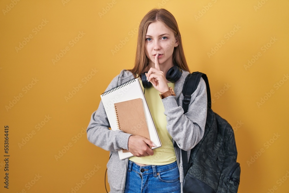 Young caucasian woman wearing student backpack and holding books asking to be quiet with finger on lips. silence and secret concept. Young caucasian woman wearing student backpack and holding books asking to be quiet with finger on lips. silence and secret concept.