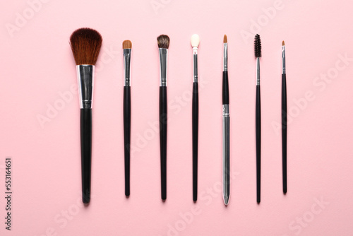 Different makeup brushes on pink background, flat lay