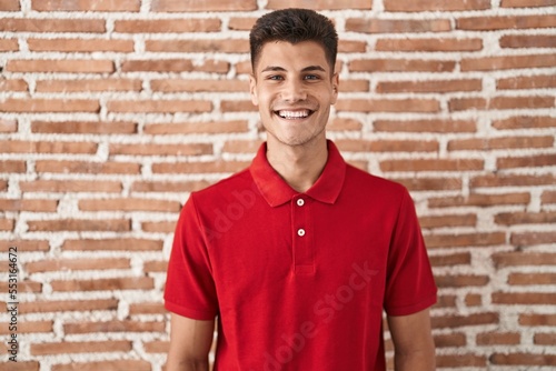 Young hispanic man standing over bricks wall with a happy and cool smile on face. lucky person.