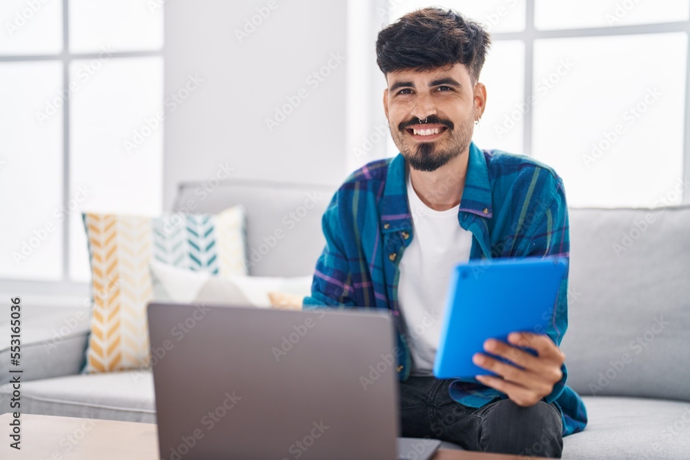 Young hispanic man using laptop and touchpad sitting on sofa at home Young hispanic man using laptop and touchpad sitting on sofa at home