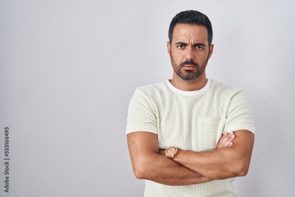 Fototapeta premium Hispanic man with beard standing over isolated background skeptic and nervous, disapproving expression on face with crossed arms. negative person.