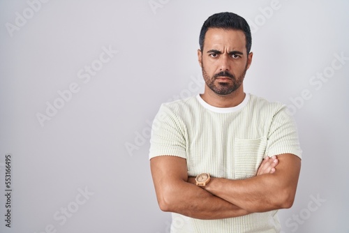 Hispanic man with beard standing over isolated background skeptic and nervous, disapproving expression on face with crossed arms. negative person.