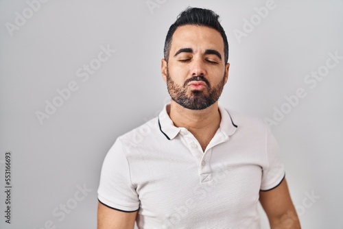 Young hispanic man with beard wearing casual clothes over white background looking at the camera blowing a kiss on air being lovely and sexy. love expression.